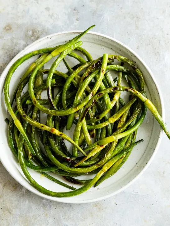 grilled garlic scapes on a plate with salt