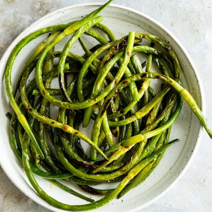 grilled garlic scapes on a plate with salt