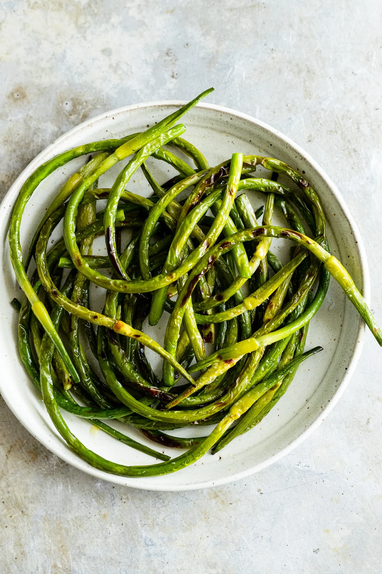 grilled garlic scapes on a plate with salt