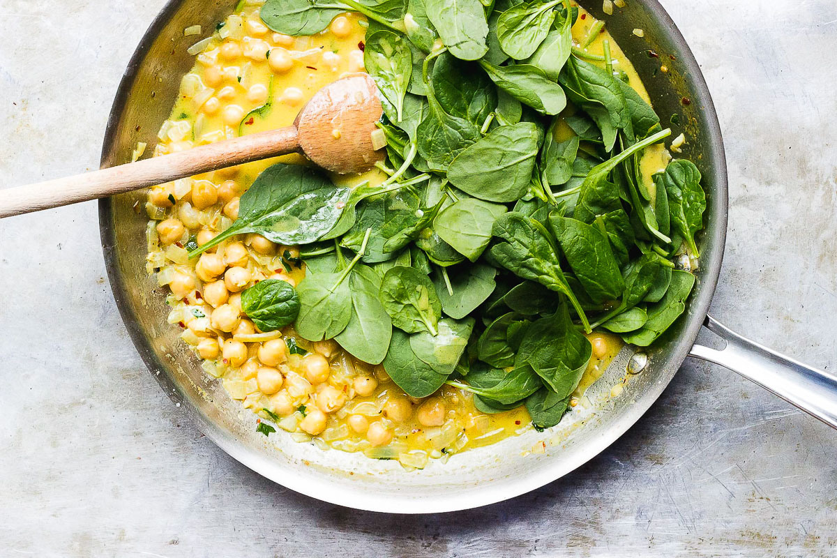 yellow curry and spinach in pot with spoon