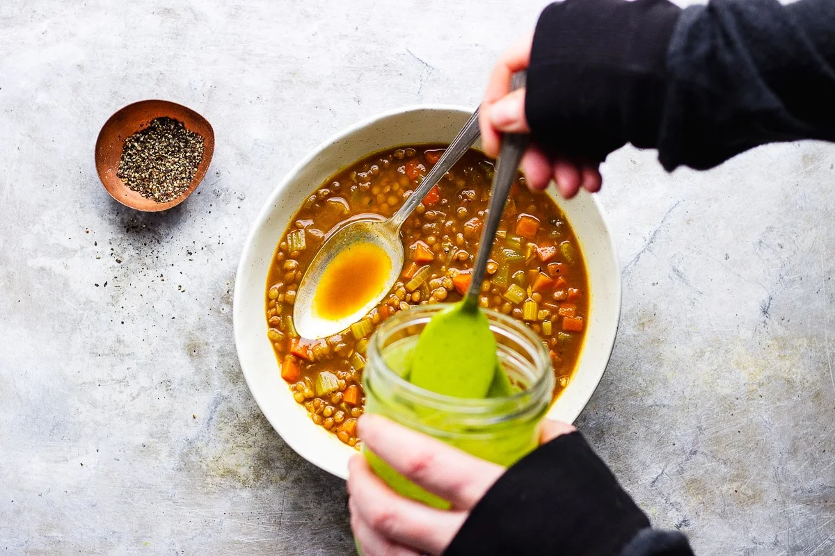 pouring parsley sauce on lentil soup