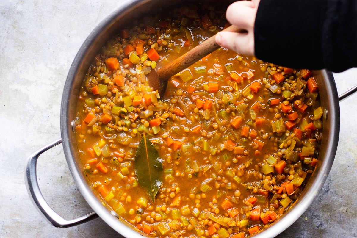 stirring a pot of vegan lentil soup