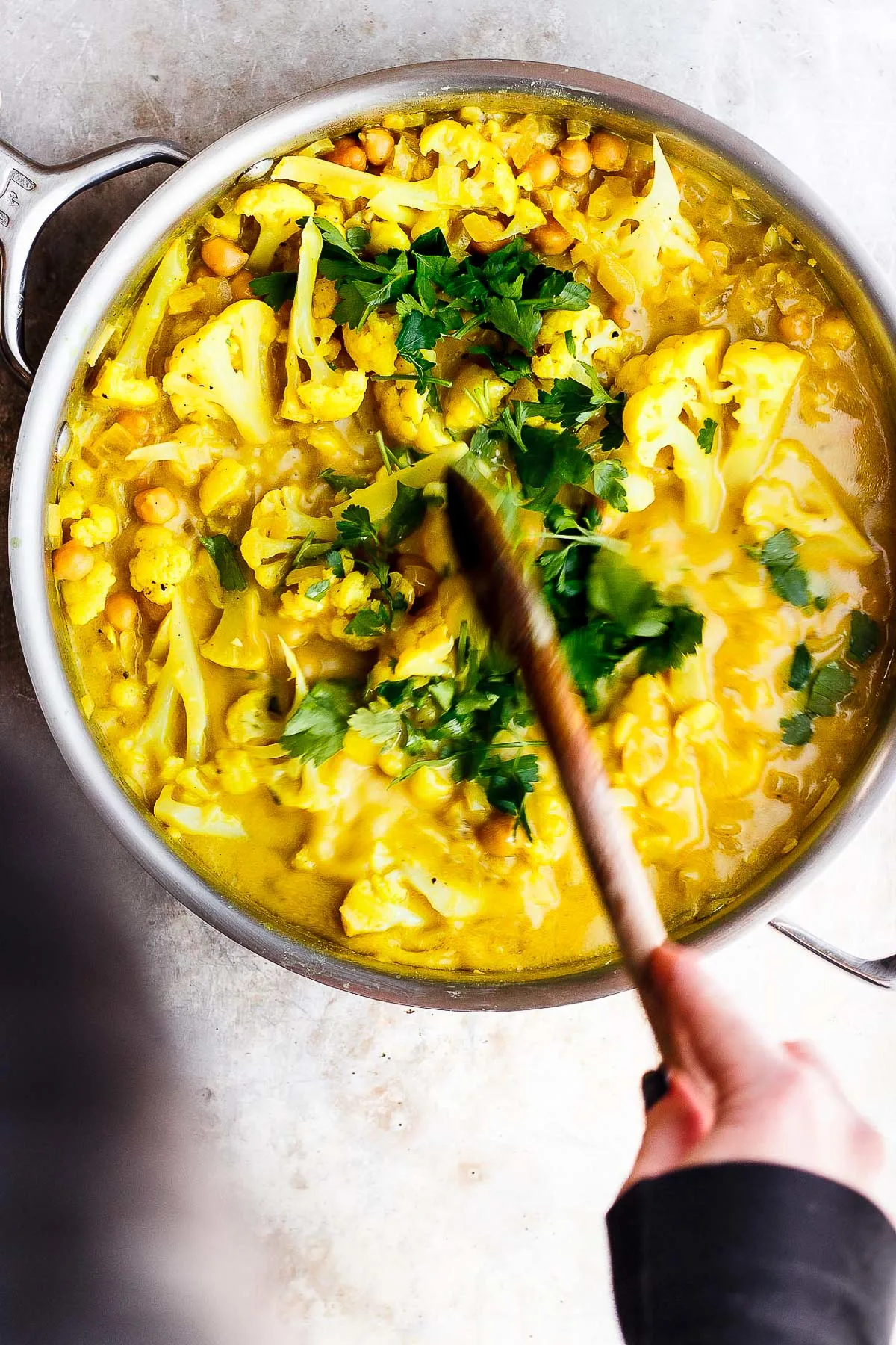 hands stirring stew with wooden spoon