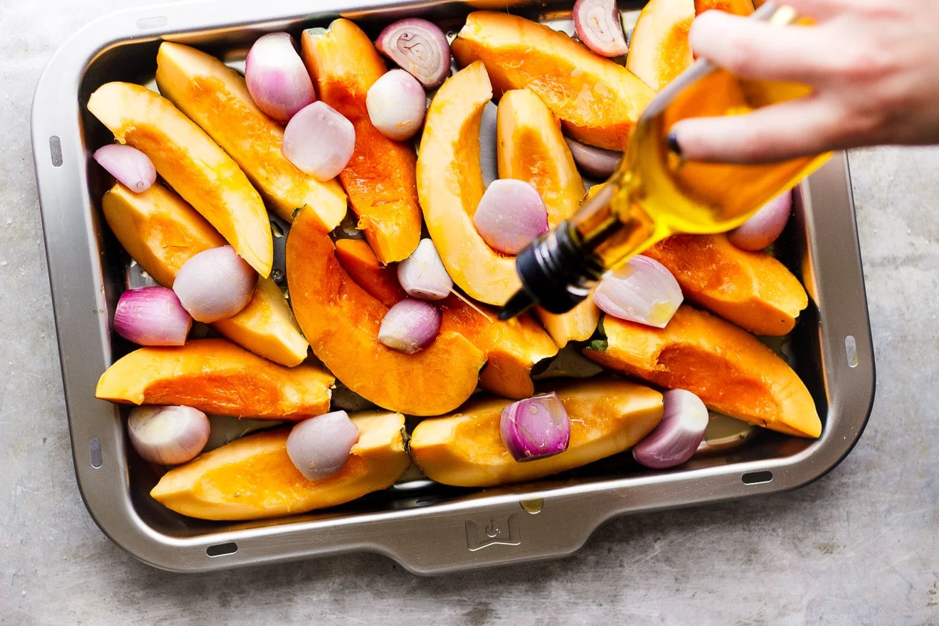 drizzling acorn squash and shallots with olive oil