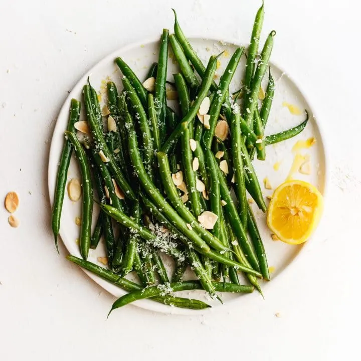lemony green beans on a plate with toasted almonds and lemon and cheese